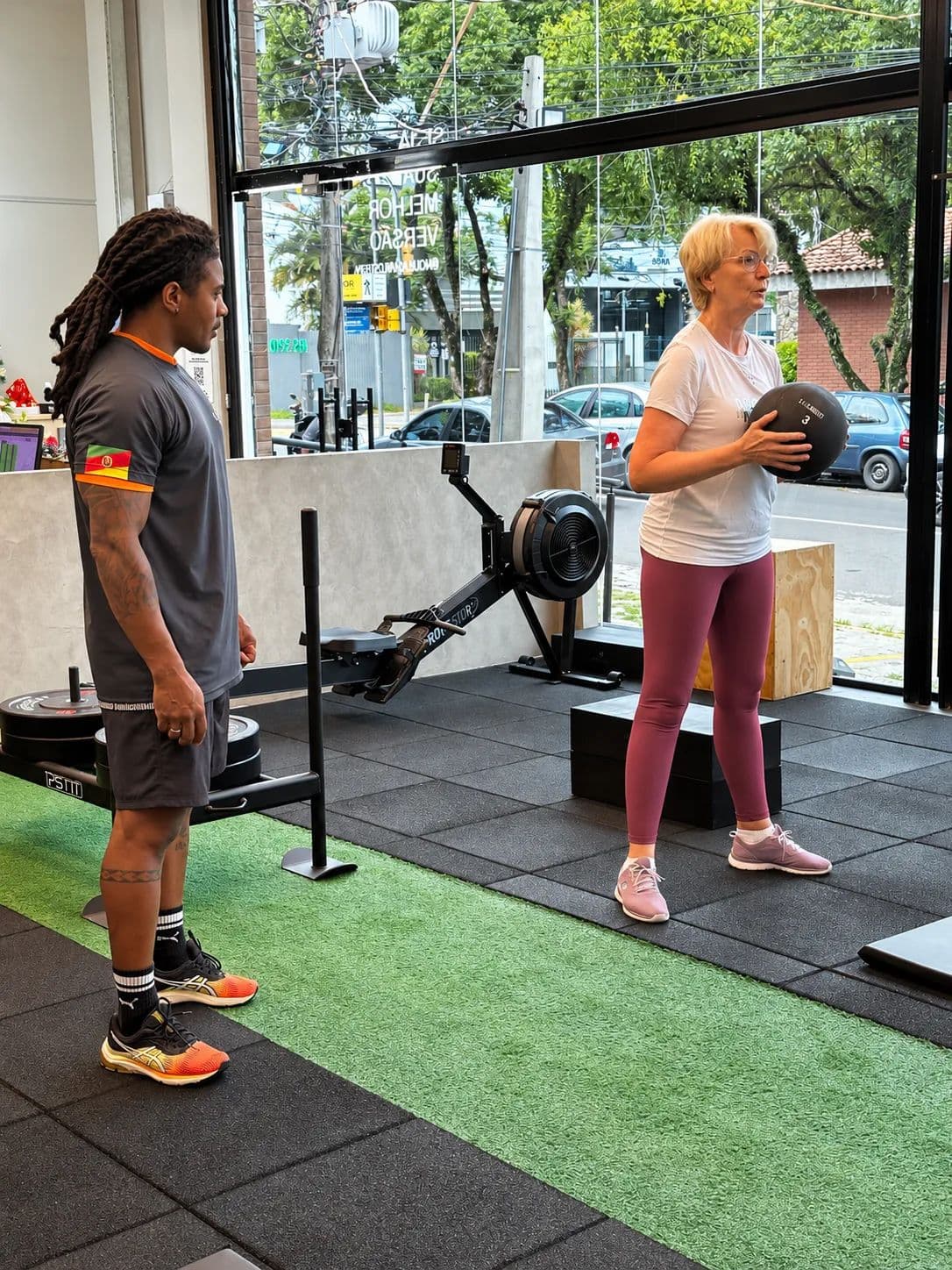 Professor acompanhando uma aluna em um exercício com bola na área de funcional