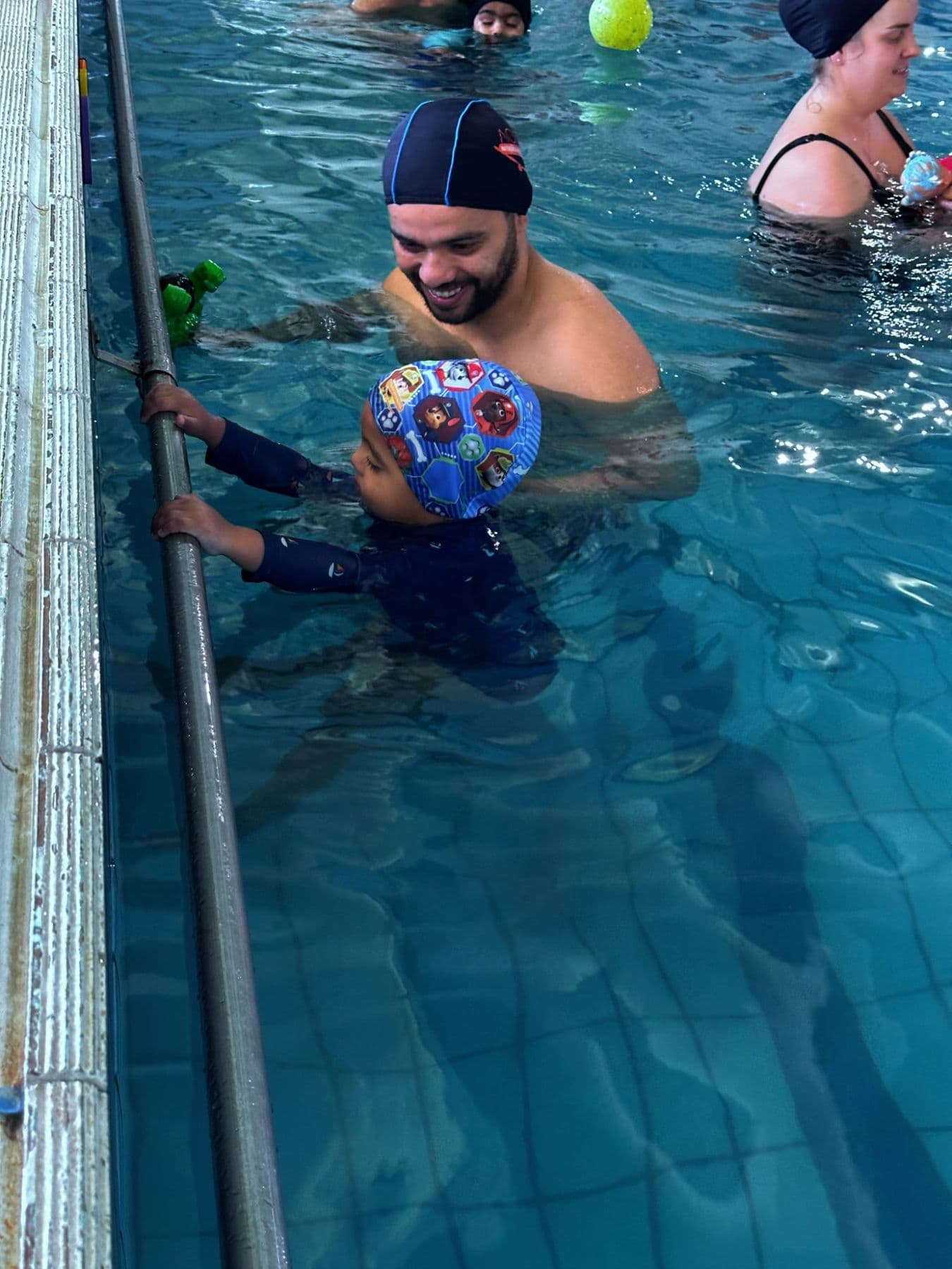Professor de natação acompanhando uma criança na borda da piscina